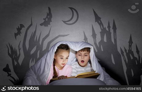 Children sitting in bed under blanket with book