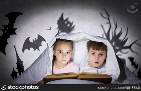 Children sitting in bed under blanket with book