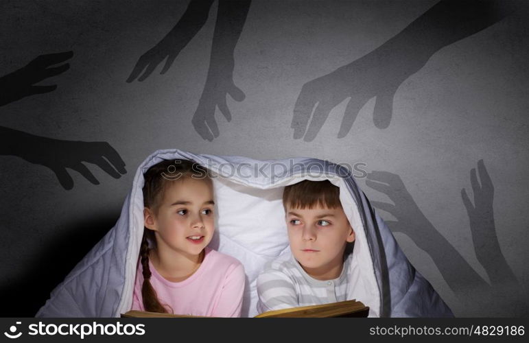 Children sitting in bed under blanket with book