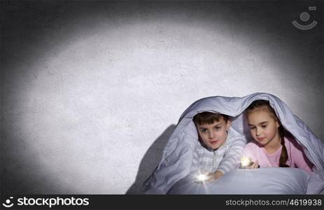 Children sitting in bed under blanket with flashlights