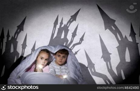 Children sitting in bed under blanket with flashlights