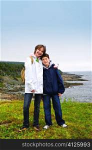 Children smiling at coastal view of rocky Atlantic shore in Newfoundland, Canada