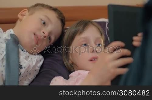 Children spending leisure with tablet computer. Girl playing game on pad and her friend watching it