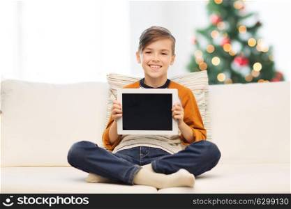 children, technology, advertisement and people concept - smiling boy with tablet pc computer at home over christmas tree background. smiling boy with tablet pc at home at christmas