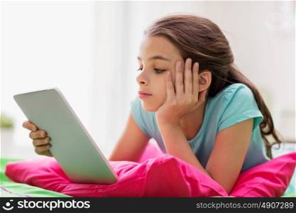 children, technology and communication concept - bored girl with tablet pc lying in bed at home. bored girl with tablet pc lying in bed at home