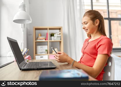children, technology and communication concept - happy smiling teenage student girl distracting from homework and texting on smartphone at home. girl with smartphone distracting from homework
