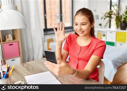 children, technology and communication concept - happy smiling teenage student girl with smartphone distracting from homework and having video call at home. girl with smartphone having video call at home
