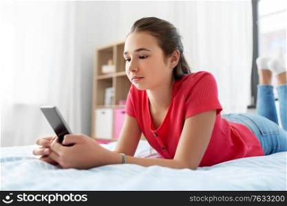 children, technology and communication concept - sad teenage girl texting on smartphone at home. sad teenage girl texting on smartphone at home