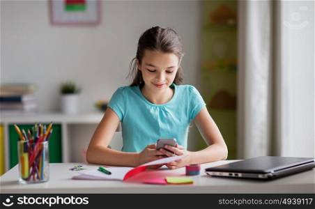 children, technology and communication concept - smiling girl distracting from homework and texting on smartphone at home. girl with smartphone distracting from homework