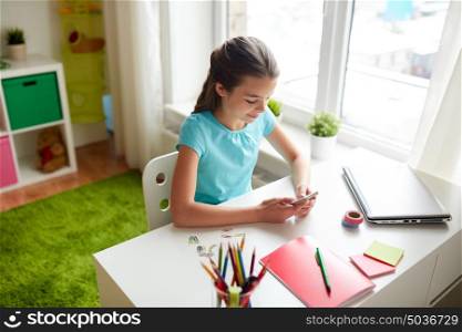 children, technology and communication concept - smiling girl distracting from homework and texting on smartphone at home. girl with smartphone distracting from homework
