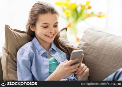 children, technology and communication concept - smiling girl texting on smartphone at home. smiling girl texting on smartphone at home. smiling girl texting on smartphone at home