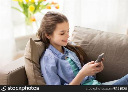 children, technology and communication concept - smiling girl texting on smartphone at home. smiling girl texting on smartphone at home