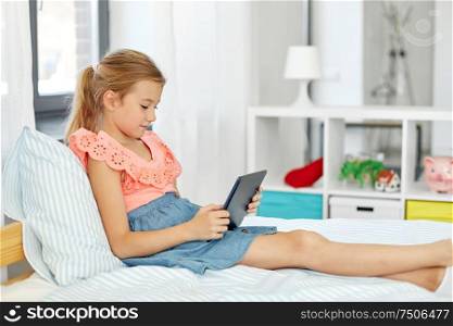 children, technology and communication concept - smiling girl with tablet computer sitting on bed at home. smiling girl with tablet pc sitting on bed at home
