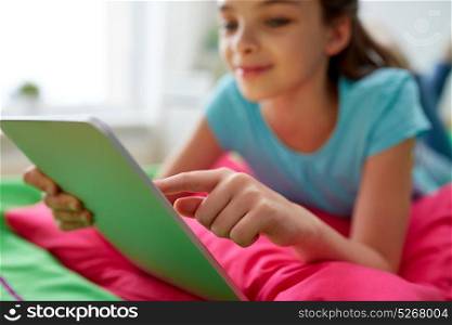 children, technology and communication concept - smiling girl with tablet pc lying on bed at home. smiling girl with tablet pc lying on bed at home
