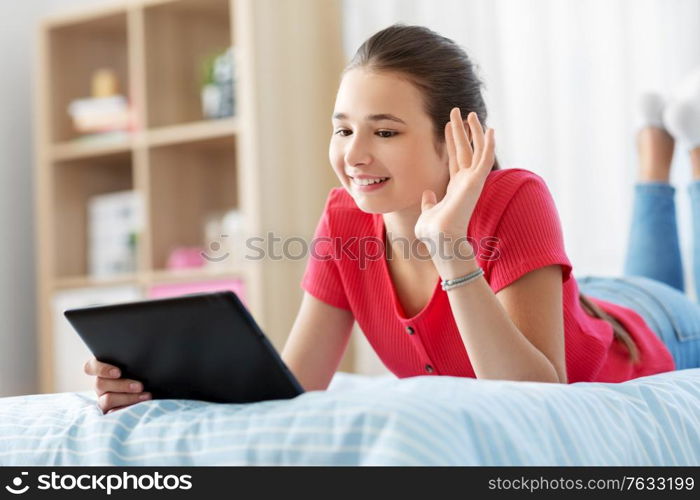 children, technology and communication concept - smiling teenage girl having vide call on tablet computer lying on bed at home. girl having vide call on tablet computer at home