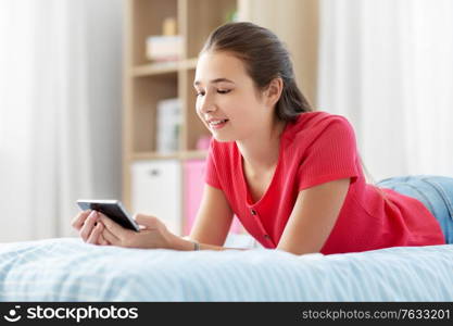 children, technology and communication concept - smiling teenage girl texting on smartphone at home. smiling teenage girl texting on smartphone at home