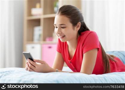 children, technology and communication concept - smiling teenage girl texting on smartphone at home. smiling teenage girl texting on smartphone at home