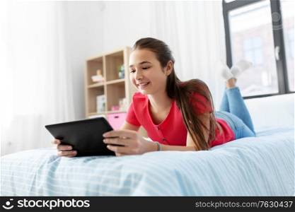children, technology and communication concept - smiling teenage girl with tablet computer lying on bed at home. smiling girl with tablet pc lying on bed at home