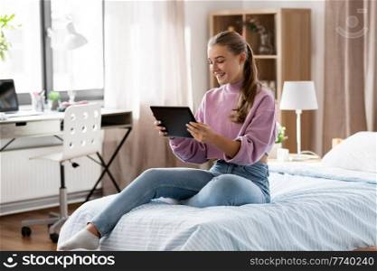 children, technology and communication concept - smiling teenage girl with tablet computer sitting on bed at home. smiling girl with tablet pc sitting on bed at home