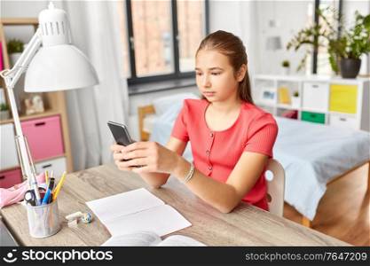 children, technology and communication concept - teenage student girl distracting from homework and texting on smartphone at home. girl with smartphone distracting from homework