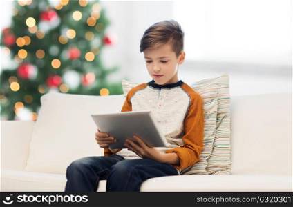 children, technology and people concept - boy with tablet pc computer at home over christmas tree background. boy with tablet pc at home at christmas