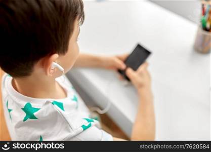 children, technology and people concept - close up of boy with smartphone and earphones listening to music at home. boy with earphones and smartphone at home
