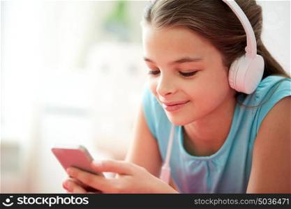 children, technology and people concept - close up of happy girl with smartphone and headphones listening to music at home. close up of girl with smartphone and headphones