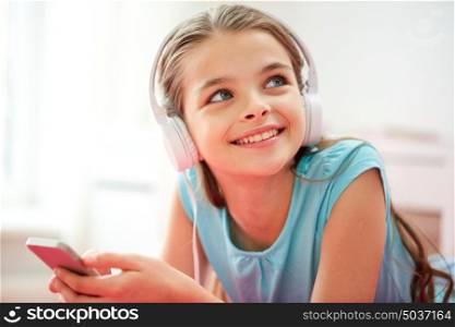 children, technology and people concept - close up of happy girl with smartphone and headphones listening to music at home. close up of girl with smartphone and headphones