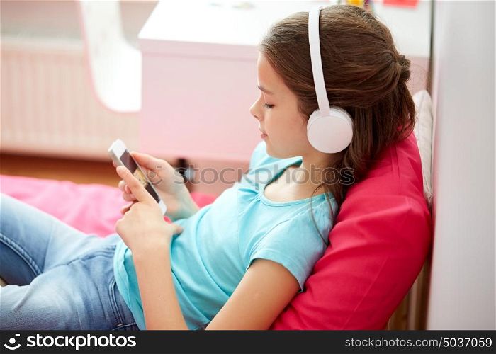 children, technology and people concept - happy girl with smartphone and headphones listening to music in bed at home. happy girl with smartphone and headphones at home