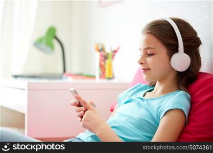 children, technology and people concept - happy girl with smartphone and headphones listening to music in bed at home. happy girl with smartphone and headphones at home