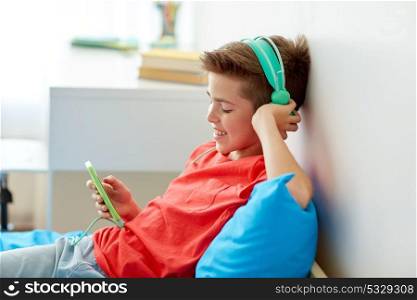 children, technology and people concept - happy smiling boy with smartphone and headphones listening to music at home. happy boy with smartphone and headphones at home