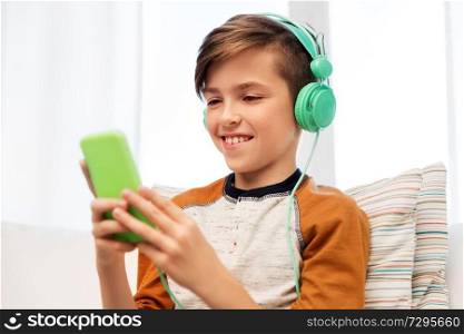 children, technology and people concept - happy smiling boy with smartphone and headphones listening to music at home. happy boy with smartphone and headphones at home