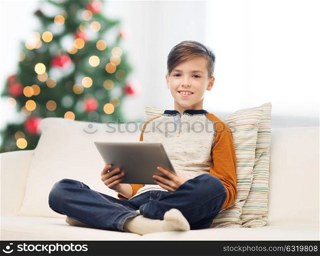 children, technology and people concept - smiling boy with tablet pc computer at home over christmas tree background. smiling boy with tablet pc at home at christmas