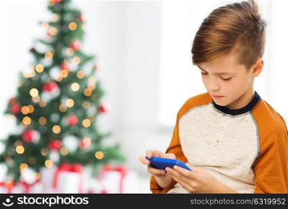 children, technology, communication and people concept - close up of boy with smartphone texting message or playing game at home over christmas tree background. close up of boy with smartphone at christmas