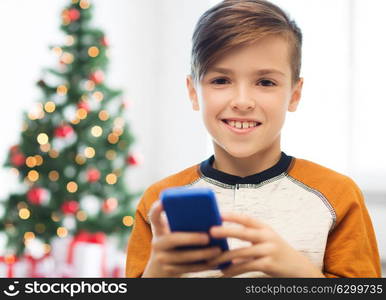 children, technology, communication and people concept - close up of smiling boy with smartphone texting message or playing game at home over christmas tree background. close up of happy boy with smartphone at christmas