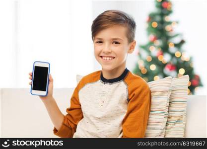 children, technology, communication and people concept - smiling boy with smartphone at home over christmas tree background. boy with smartphone at home at christmas