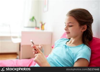 children, technology, people and communication concept - smiling girl texting on smartphone or playing game at home. smiling girl texting on smartphone at home