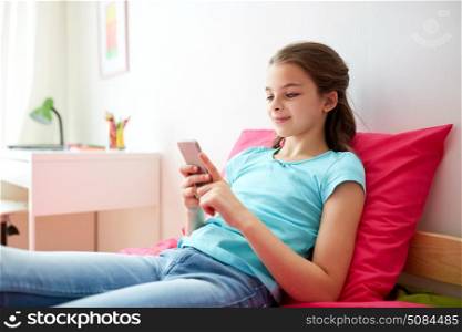 children, technology, people and communication concept - smiling girl texting on smartphone or playing game at home. smiling girl texting on smartphone at home. smiling girl texting on smartphone at home
