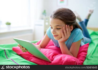 children, technology, people and communication concept - smiling girl with tablet pc lying in bed at home. smiling girl with tablet pc lying in bed at home
