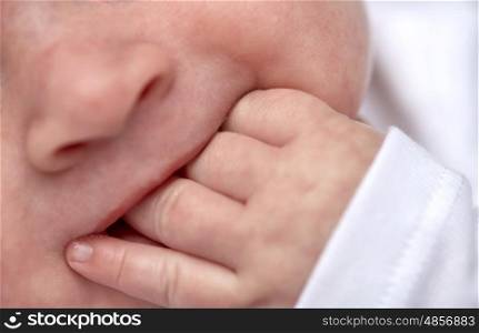 children, teething and people concept - close up of baby sucking his fingers