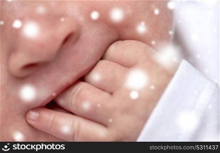 children, teething and people concept - close up of baby sucking his fingers over snow. close up of baby sucking his fingers