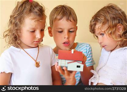 children three together keeping in hands model of house in cosy room, two pretty girls and boy