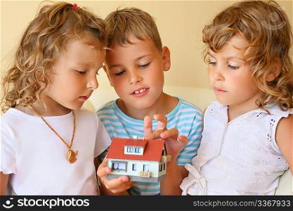 children three together keeping in hands model of house in cosy room, boy touches house finger