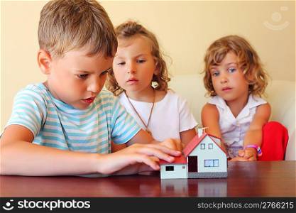 children three together looking at model of house standing on table in cosy room