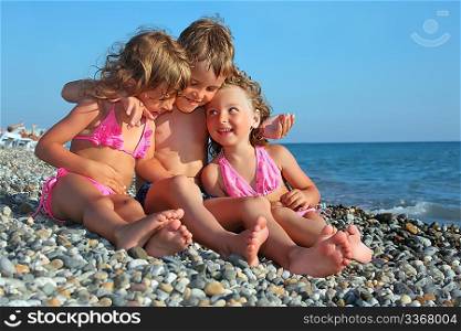 children three together sitting on stony beach