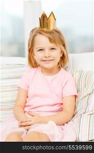 children, toys and happiness concept - smiling little girl in crown sitting on sofa at home