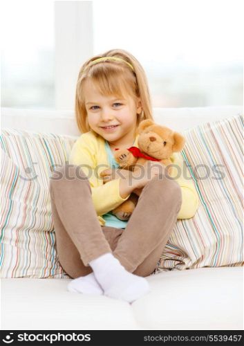 children, toys and happiness concept - smiling little girl with teddy bear sitting on sofa at home