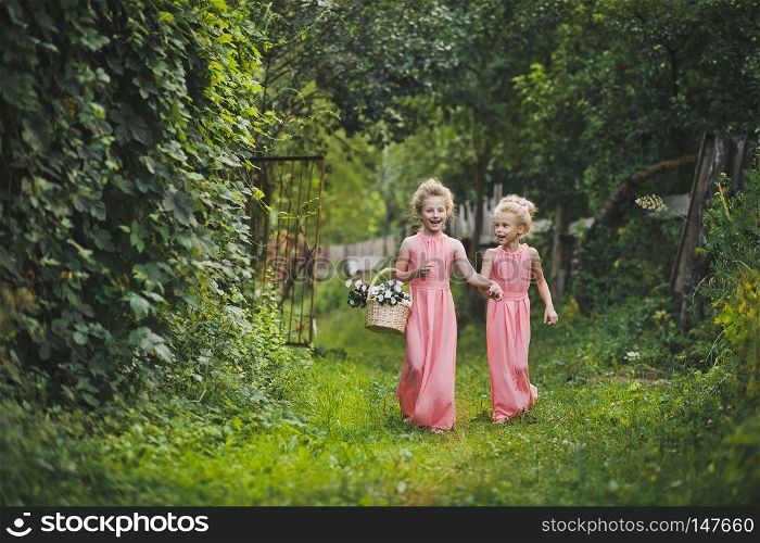 Children walk along the summer garden.. The kids in long pink gowns walking down the garden alley 6583.
