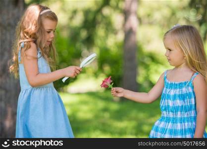 Children with a magnifying glass. Two little sisters of friends looking through magnifier at flower