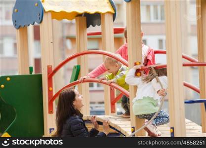 Children with mother are playing at the playground outdoors